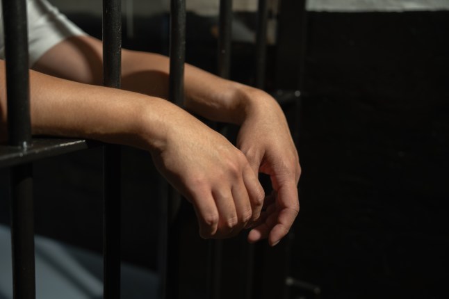 Hands of a prisoner in a cell behind bars.