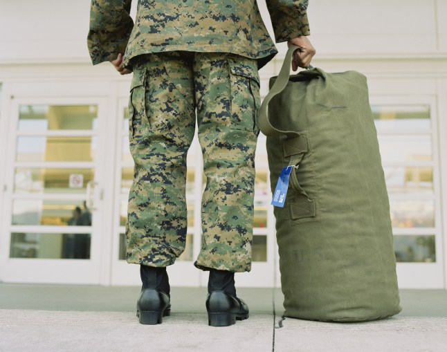 A soldier faces airport doors with a khaki bag