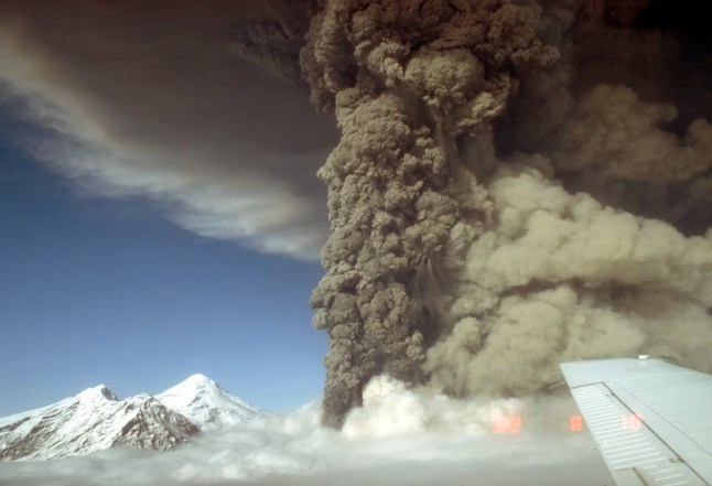 Aerial view, looking north, of the eruption column from the Crater Peak vent on Mount Spurr volcano on Aug. 18, 1992. A light-tan cloud ascending from pyroclastic flows is visible at right. The 11,070-foot-high summit lava dome complex of Mount Spurr is visible at left.