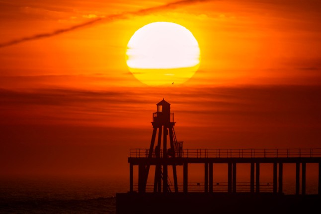 ?? Licensed to London News Pictures. 11/04/2025. Whitby UK. The sun rises this morning over the West light house in Whitby harbour on the Yorkshire coast. Photo credit: Andrew McCaren/LNP