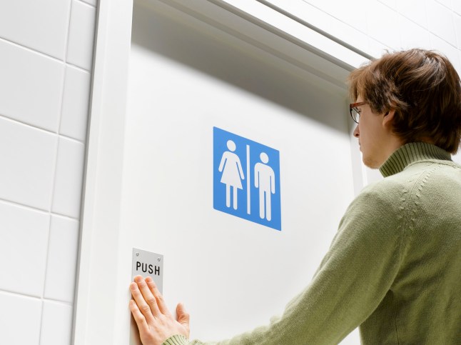 A man entering a toilet with a male and female sign on it