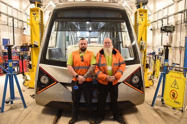 Train driver father-and-son duo standing in front of the Coventry very light rail train carriage.