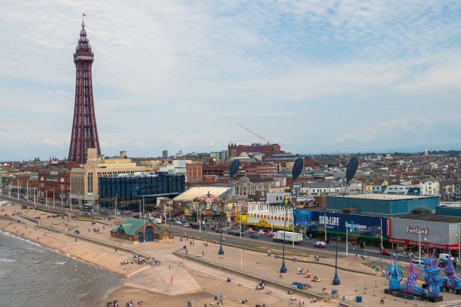 Blackpool, Lancashire, United Kingdom - 27 July 2024 : aerial view of the seafront at Blackpool with the north pier and tower surrounded by seafront buildings and people on the beach in summer