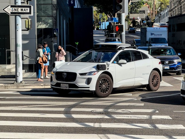 Los Angeles, California-December 26, 2024: A Waymo autonomous taxi picks up passengers in Downtown Los Angeles. The City of LA allows for self driving taxis driven by AI and Lidar Sensors under a pilot program.