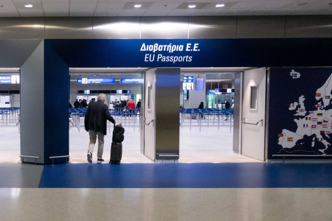 An arrival gate at Athens International Airport with a man pulling his luggage through the gate.