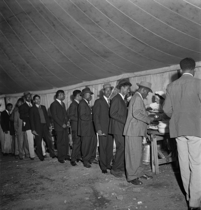 Jamaican men, who arrived in Britain on HMT Empire Windrush on 22nd June, line up in a canteen marquee on Clapham Common to get a meal, London, June 1948. For two shillings and sixpence a week they get food and a bed in a converted air-raid shelter under nearby Clapham South Underground station. (Photo by Chris Ware/Keystone Features/Hulton Archive/Getty Images)