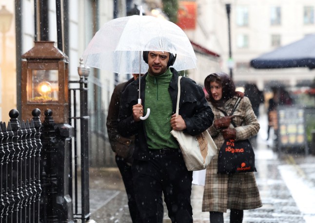 A man shelters under his umbrella as a hail storm falls in London, Britain, March 13, 2025. REUTERS/Isabel Infantes