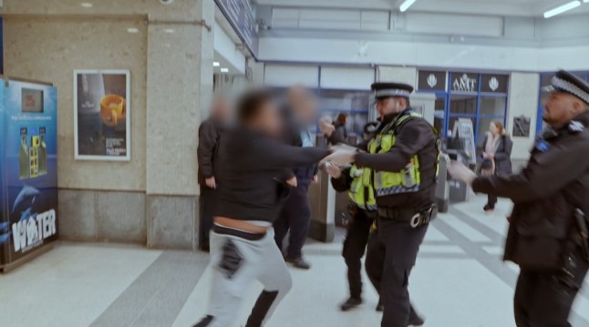 A suspected fare dodger with his face blurred held up by police officers at a Tube station.