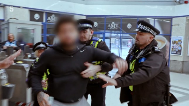 A suspected fare dodger with his face blurred held up by police officers at a Tube station.