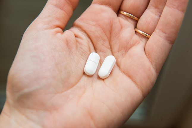 Close-up view of a hand holding two white pills in the palm above a blurry background