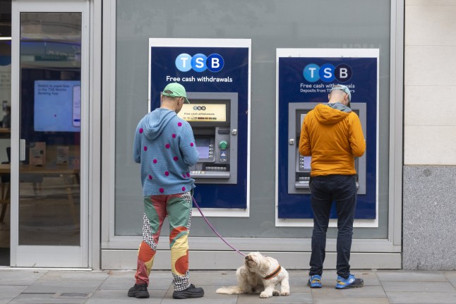 Customers at automated teller machines (ATMs) outside a bank branch of TSB Bank Plc, Banco Sabadell's subsidiary in the UK.