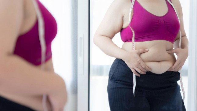 Overweight woman checking belly fat in front of mirror with measuring tape, wearing sportswear, body image concern, weight loss motivation, fitness journey, health awareness, self care concept