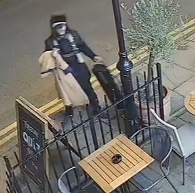 CCTV footage still of a suspect in the theft of the £150,000 violin, standing on the pavement next to a pub table and signage.