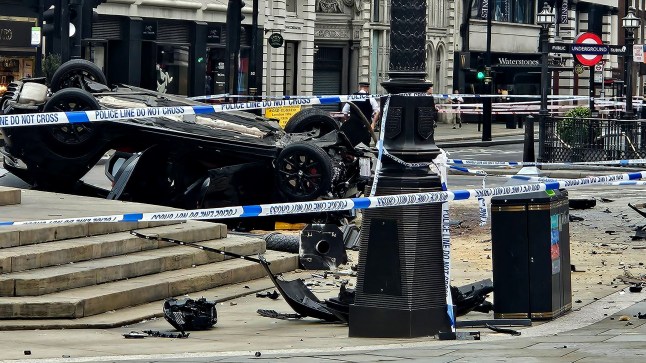 The car flipped onto its roof beside the fountain, with the roundabout and nearby roads closed.