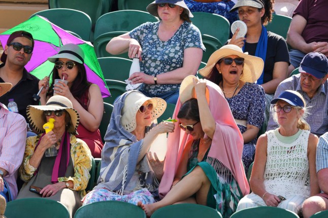 Tennis supporters use fans and water spray to cool during the Wimbledon Tennis Championships in London, Monday, June 30, 2025. (AP Photo/Kirsty Wigglesworth)