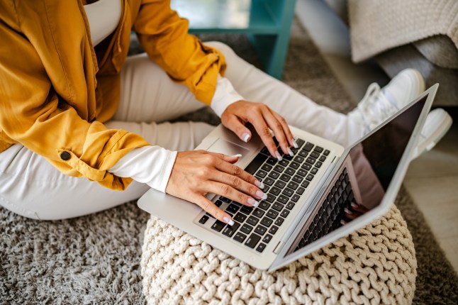 Working woman uses laptop while sitting on cosy floor in a well-lit living space.
