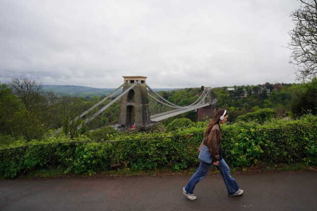 A woman walks past the Clifton Suspension Bridge which spans the Avon Gorge and the River Avon, linking Clifton in Bristol to Leigh Woods in North Somerset. Picture date: Monday April 21, 2025. PA Photo. See PA story WEATHER Easter. Photo credit should read: Ben Birchall/PA Wire