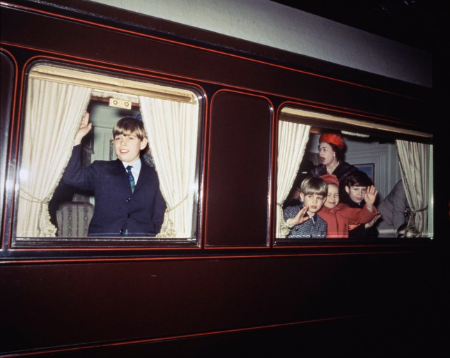 Prince Andrew waving from a window at left, with Queen Elizabeth II (1926 - 2022), Prince Edward, Lady Sarah Chatto and Viscount Linley shown in another window of the royal train at right, circa December 1965. (Photo by Fox Photos/Hulton Archive/Getty Images)