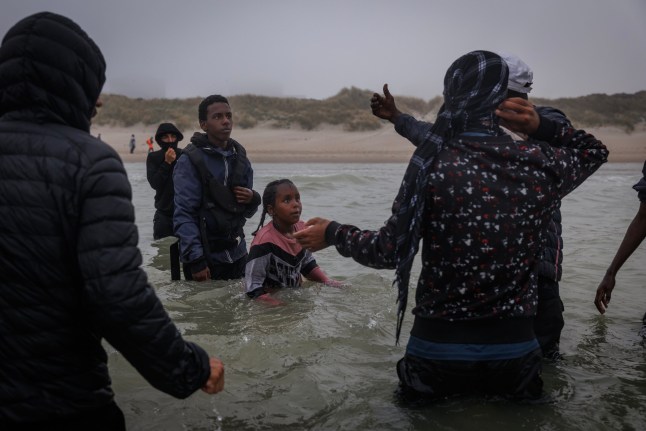 GRAVELINES, FRANCE - JULY 02: Two children try to make their way past traffickers (covering their faces) to a small boat on July 02, 2025 in Gravelines, France. The pair were unsuccessful in boarding and made their way back to the shore to try another day. The boat had arrived through the fog, already very full of migrants who had boarded further down the coast, looking to squeeze a few more people in. Last month, it was reported that French officials were planning changes to policies that govern interceptions at sea, allowing police to intercept small boats within 300 metres of the French shoreline, in a bid to curb migrant crossings of the English Channel. The move, which has not been confirmed, would be welcomed by UK authorities, who see it as a step toward stronger border enforcement. (Photo by Dan Kitwood/Getty Images)