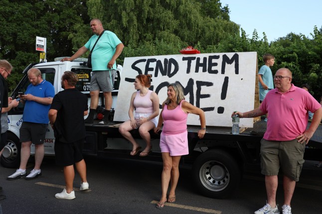 ? Licensed to London News Pictures. 13/07/2025. Epping, UK. Local residents gather next to a sign reading ?SEND THEM HOME!? as they hold a protest outside The Bell hotel in Epping, Essex, England, against the hotel?s housing of migrants. Protesters and parts of the local community are raising concerns about an alleged sexual assault carried out by a migrant in Epping last week. Photo credit: Jacqueline Lawrie/LNP