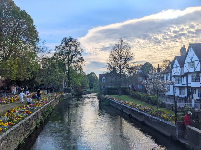 Canterbury, UK - April 19 2025: The River Stour flows through the historic city past traditional Tudor style buildings and banks lined with people enjoying colorful spring flowers at Westgate Gardens