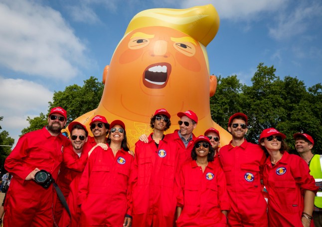 The Trump Baby sitting team dressed in red boiler suits in front of the six metre high inflatable TrumpBaby before his flight above Parliament Square, London, United Kingdom. 13th July 2018. (photo by Andy Aitchison / Trump Babysitter)