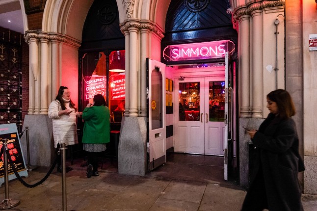 A commuter passes customers outside a Simmons Bar in the City of London, UK, Tuesday, Nov. 7, 2023. City center pubs, still in recovery mode in the post-Covid era, face sliding revenue and rising costs. Photographer: Jose Sarmento Matos/Bloomberg via Getty Images