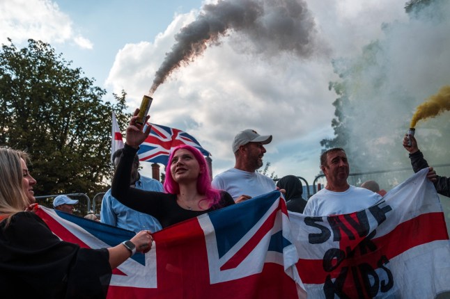 EPPING, ENGLAND - JULY 31: People hold flares during a protest outside The Bell Hotel on July 31, 2025 in Epping, England. Anti-migrant protesters, as well as counter-protesters, have organised rallies in Epping near the Bell Hotel, which is being used as migrant accommodation. A series of protests have taken place here following the arrest of an asylum seeker on suspicion of alleged sexual assaults in the town. (Photo by Carl Court/Getty Images)