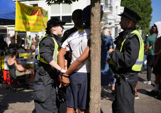 A young man is handcuffed by a police officer, but after being questioned and search was released, at the Notting Hill Carnival celebration in west London over the Summer Bank Holiday weekend. Picture date: Monday August 25, 2025. PA Photo. Photo credit should read: Yui Mok/PA Wire