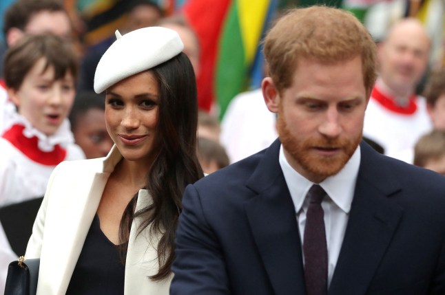 Britain's Prince Harry (R) and Meghan Markle leave after attending a Commonwealth Day Service at Westminster Abbey in 2018. Harry is wearing a dark suit and white shirt. Meghan is wearing a white jacket and matching white beret-style hat.