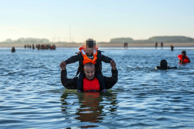 GRAVELINES, FRANCE - AUGUST 25: A man carries a boy on his shoulders as migrants wade into the sea to try and board a dinghy into the English Channel on August 25, 2025 in Gravelines, France. Migrant crossings by boat have caused much controversy in the UK, with far-right groups organising demonstrations outside hotels housing migrants across the country over the summer. As of late August 2025, more than 28,000 migrants have crossed the English Channel in small boats this year. (Photo by Carl Court/Getty Images)