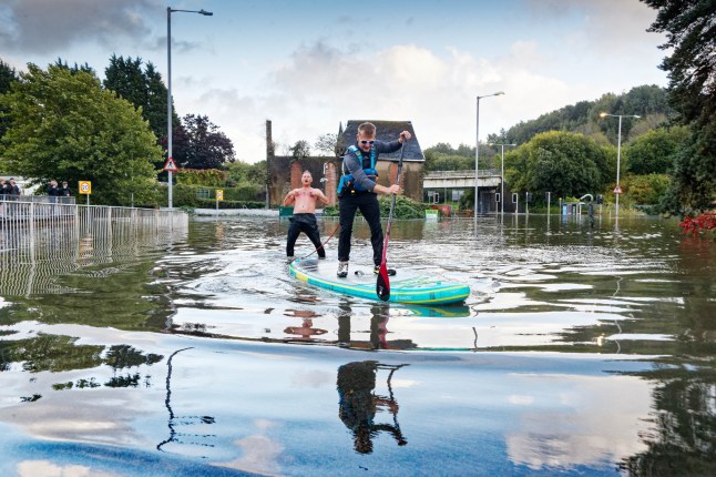 Pictured: A young man paddleboards along with another man in the flood water at Cwmbwrla roundabout in Swansea. Sunday 14 September 2025 Re: Heavy rain causes flash flooding during which drivers had to be rescued from their submerged cars at Cwmbwrla roundabout, Swansea, Wales, UK.